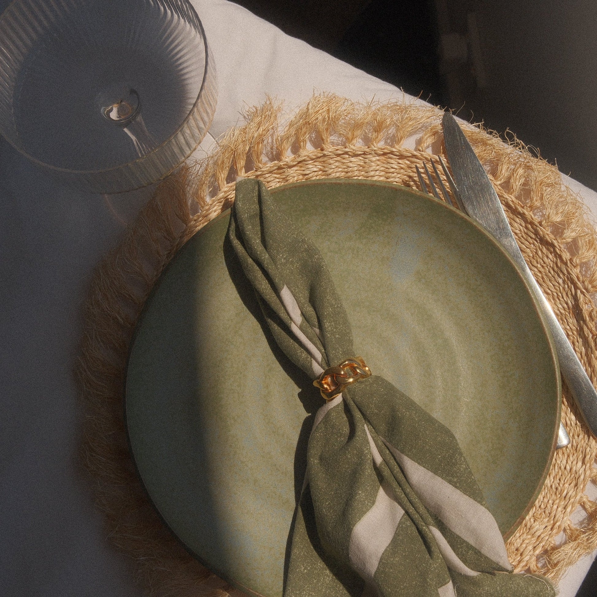 Green plate with a cloth napkin and cutlery on a marble surface