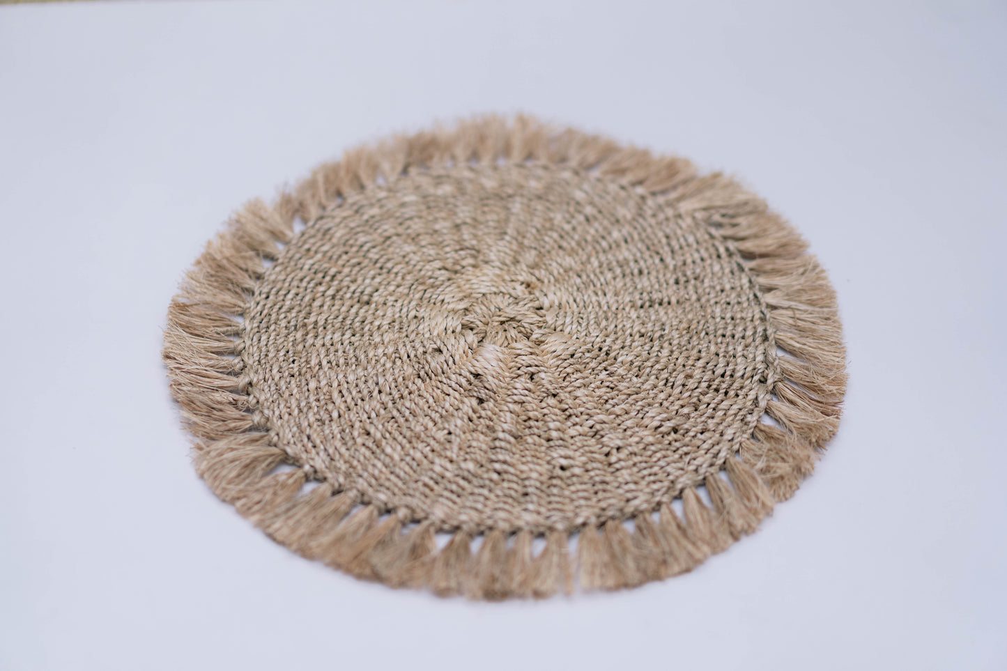 Round woven placemat with tassels on a light gray background