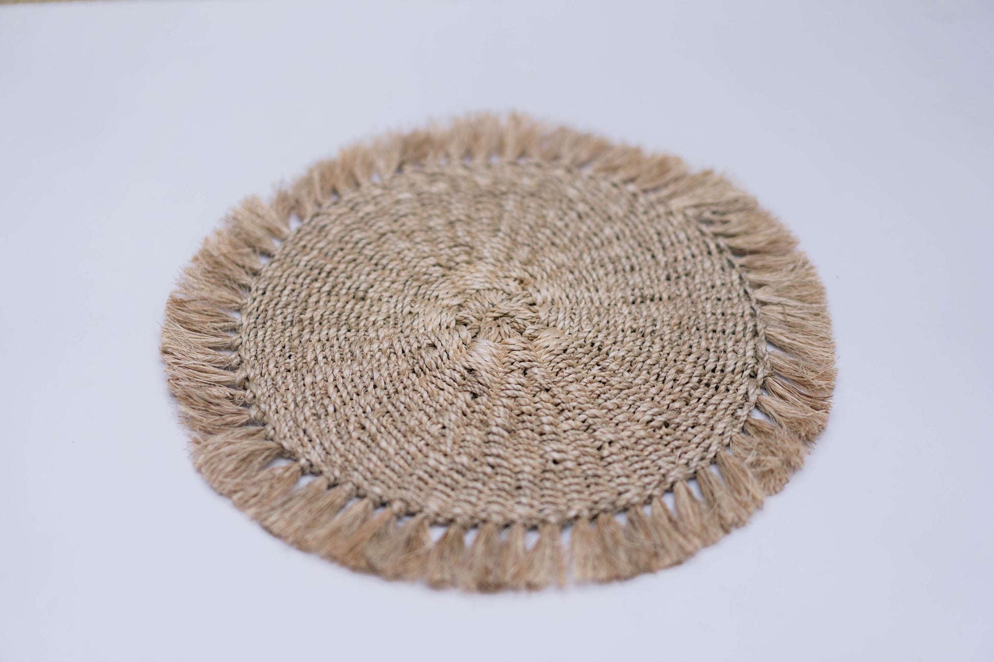 Round woven placemat with tassels on a light gray background